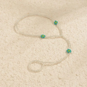 Detail of bohemian white seed bead hand chain with blue flower accents on textured background