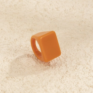 Gros plan d'une bague carrée large en résine orange avec une finition lisse et brillante