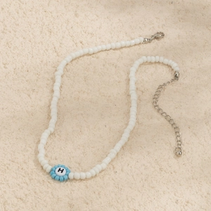Primer plano de collar de cuentas blancas con flor azul y colgante de letra H