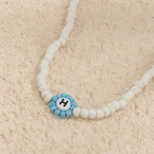 Primer plano de un collar de cuentas hecho a mano con flor azul y dije de letra H
