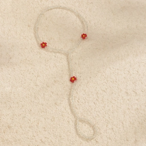 Ethnic style beaded barefoot sandal with white beads and red daisy flowers on sand texture
