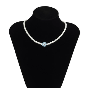 Detalle del collar de cuentas blancas con colgante de flor azul claro y la letra H