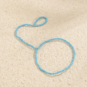 Dettaglio di una cavigliera boho fatta a mano con perline azzurre su fondo rustico