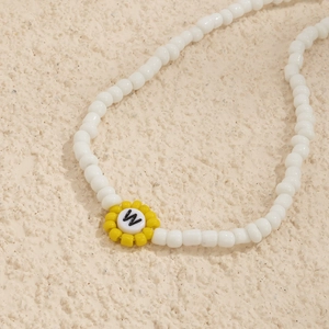 Detalle de collar de cuentas blancas con un colgante de margarita amarilla y la letra W