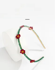 Close-up of a gold metal headband with woven green beads and red daisy flower details