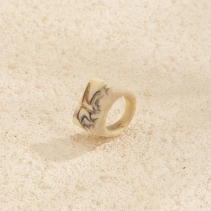 Gros plan d'une bague géométrique carrée en résine avec texture marbre crème élégante