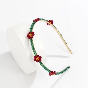 Detail of beaded daisy headband with red and green crystals on golden frame