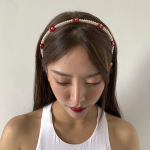 Macro detail of white faux pearl headband with red acrylic daisy flowers and gold center beads