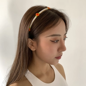 Close-up of white imitation pearl headband with orange daisy flowers worn by a model