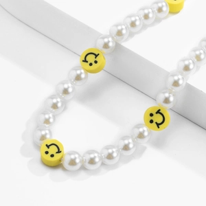 Macro detail of beaded phone strap with white pearls and yellow smiley face beads