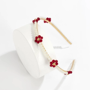 Detail of metal headband featuring red glass daisies and white faux pearls on white stand