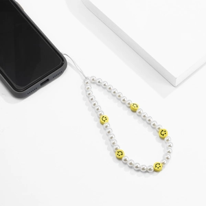 Détail de la dragonne de téléphone avec perles blanches et charms smiley jaunes