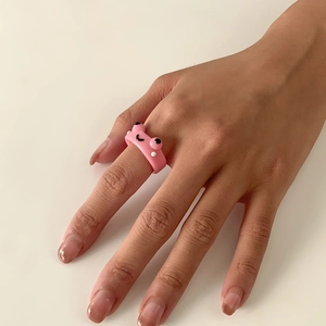Nahaufnahme eines süßen rosa Froschrings aus Harz mit Cartoon-Lächeln am Finger