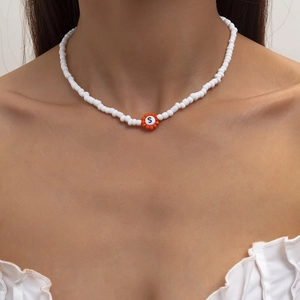 Detalle de collar de cuentas con flor naranja y letra S en el cuello de una modelo