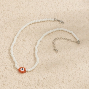 Detalle de collar de cuentas con colgante de flor naranja y letra S en el centro