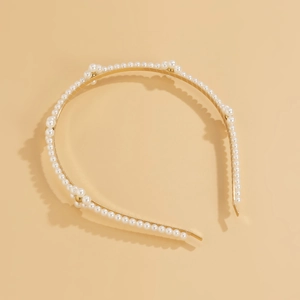 Detail of gold metal headband with white pearls forming cat ear shapes on beige background
