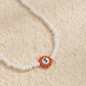 Vista macro de collar de cuentas con detalle de flor naranja y dije con la letra S