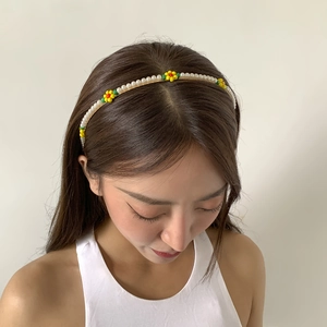 Detail shot of a slender metal headband with white pearls and colorful beaded daisy flowers
