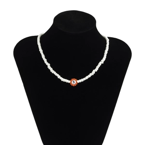 Detalle de collar de cuentas blancas con colgante de flor naranja y letra S central
