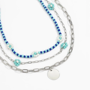 Detailopname van drielaagse kralenketting met blauwe bloemen en zilveren hangers