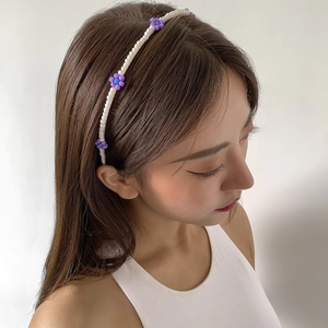 Detail of beaded headband with white pearls and purple daisy charms on brown hair