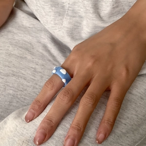 Detail eines hellblauen Harzrings mit weißen 3D-Wolken am Finger getragen