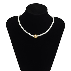 Detalle de collar de cuentas blancas con colgante de flor de corazón dorado en busto