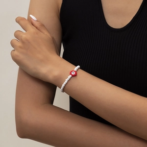 Detalle de pulsera de cuentas en la muñeca con dije de pétalo rojo y letra A blanca central