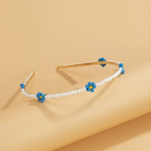 Detail of hand-woven white beaded headband with blue daisy flowers and gold frame