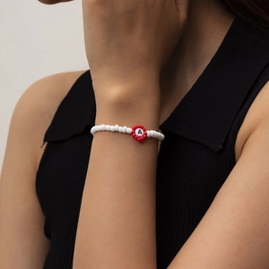 Detalle de pulsera de cuentas blancas con flor roja y un dije con la letra A grabada
