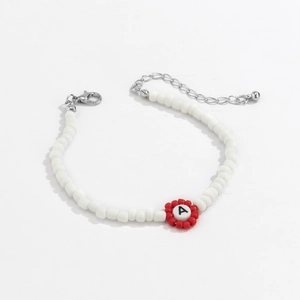 Detalle de pulsera de cuentas blancas con un dije de la letra A y cuentas rojas