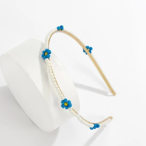 Close-up of golden metal headband with white beads and blue daisy flower ornaments