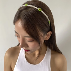 Detail of thin gold headband featuring white pearls and green resin flower ornaments