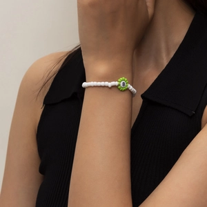 Primer plano de pulsera artesanal de cuentas blancas con flor verde y letra B central