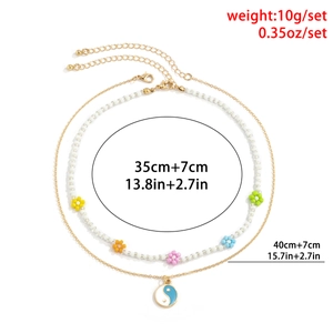 Detail van gelaagde bloemenkralenketting en gouden ketting met Yin Yang-hangers