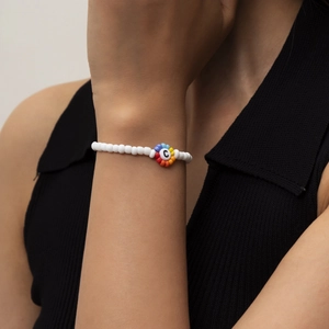 Primer plano de una pulsera de cuentas blancas con un dije de letra C de colores en la muñeca