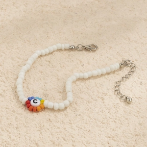 Detalle macro de pulsera bohemia con flores de arcoíris y dije de la letra C