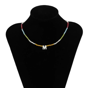 Detail van kleurrijke kralenketting met witte schelpmeter M op een zwarte buste