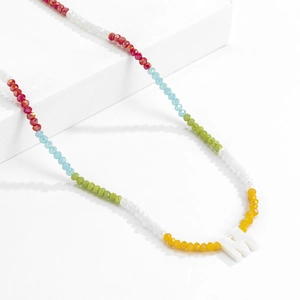 Detail van kleurrijke kralenketting met een witte letter M schelp hanger op podium