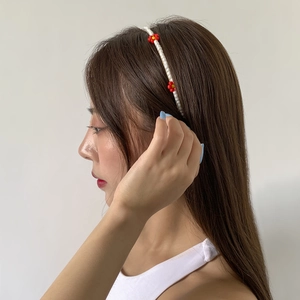 Detailed side view of a handmade white beaded headband with small red floral accents