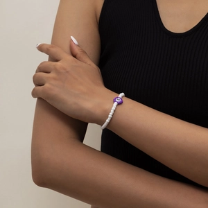 Primer plano de pulsera de cuentas blancas con colgante de flor violeta y letra E en la muñeca