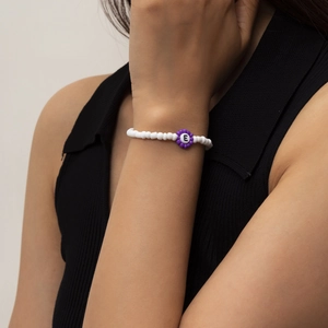 Detalle de pulsera de cuentas con una flor morada y un dije con la letra E