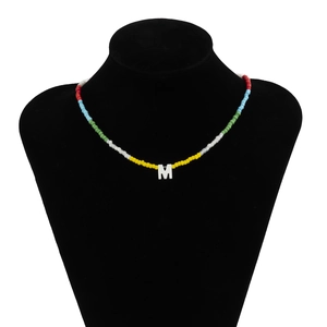 Detail van kleurrijke kralenketting met een witte letter M hanger op zwarte buste