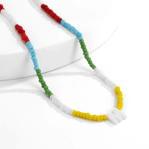 Detail van de kleurrijke boho kralenketting met een witte hars letter M hanger
