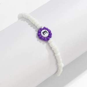 Detalle de pulsera de cuentas de colores con amuleto de flor y cuenta con letra E