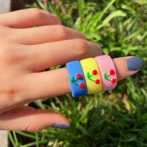 Buntes Ring-Set aus Harz mit Kirsch-Motiv in Blau, Gelb und Rosa auf natürlichem Gras
