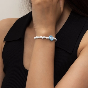 Primer plano de pulsera de cuentas blancas con flor azul y letra H usada en la muñeca