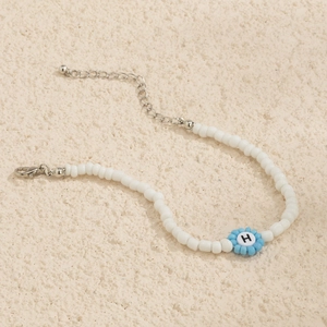 Detalle de collar de cuentas con flor azul y letra H sobre fondo de piedra con cierre