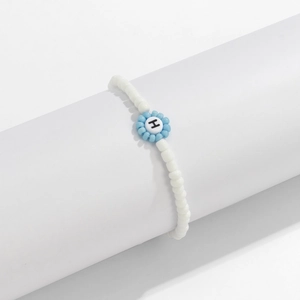 Detalle de una pulsera de cuentas con una flor azul y una cuenta blanca con la letra H