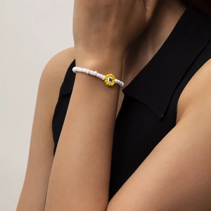 Primer plano de pulsera de cuentas blancas y una flor amarilla con la letra W